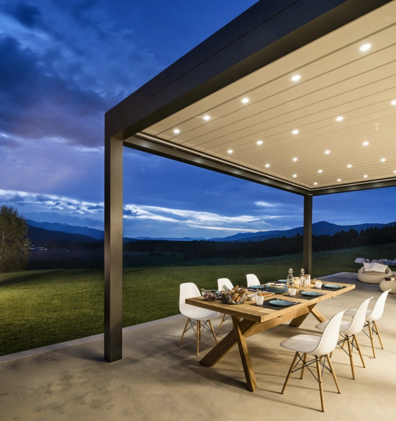 Moderní osvětlená pergola s jídelním stolem na venkově.