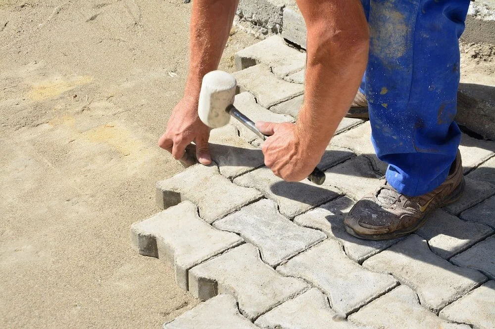 Rukou klademe betonovou dlažbu do písku pomocí gumového mlátka.