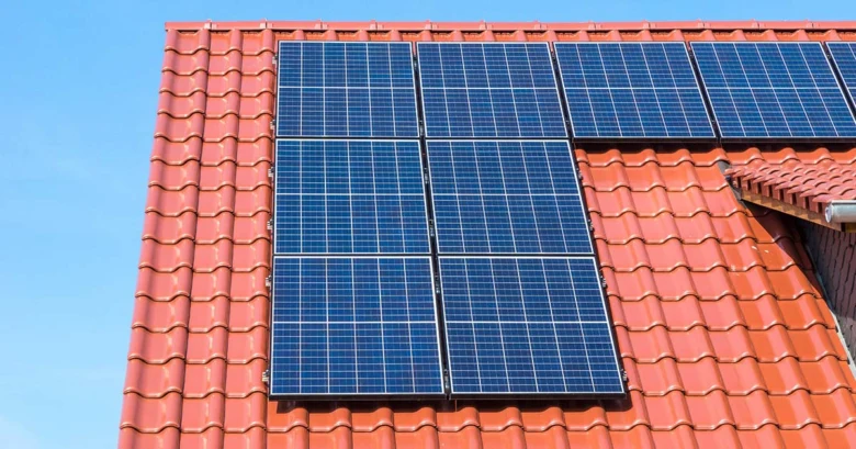 Modré fotovoltaické panely na červené taškové střechě domu.