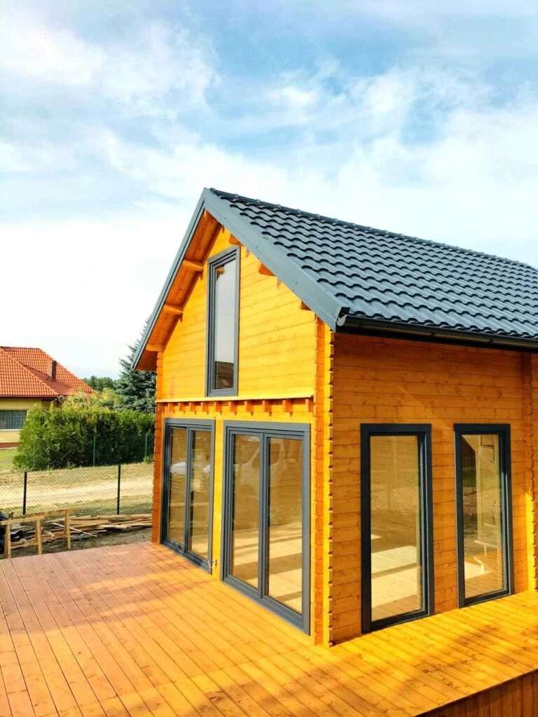 Moderní dřevěná chata s velkými okny a tmavou střechou.