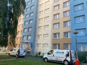Fasáda bytového domu s barevnými nátěry před parkovaným vozem.