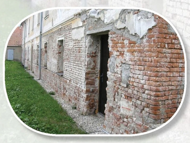 Zničená fasáda s odlupující se omítkou odhalující cihlový zdivo.