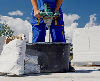 Stavebník míchá suchou betonovou směs v kbelíku.
