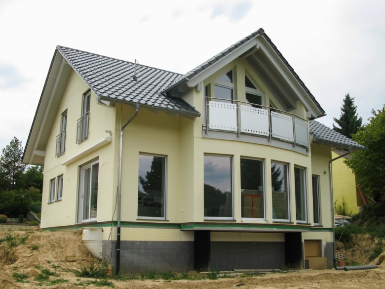 Nově postavený dům s žlutou fasádou na pozadí holé země.