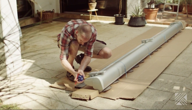 Muž měří komponentu markýzy na balkóně při instalaci.