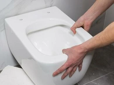Muž instaluje bílý záchod do koupelny.