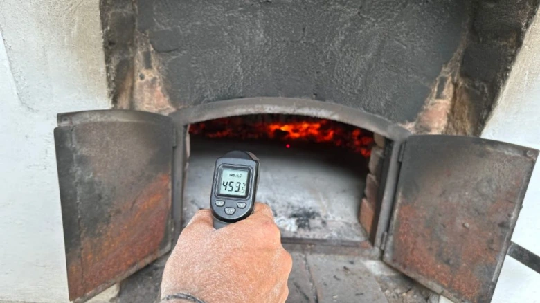 Ruční měření teploty v peci na chleba infračerveným teploměrem při hořícím ohni.