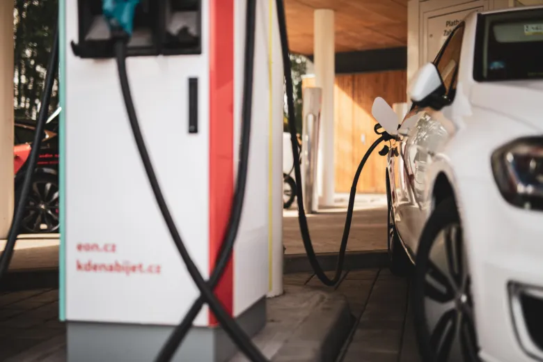 Bílé elektromobil nabíjený na veřejné elektrické čerpací stanici.