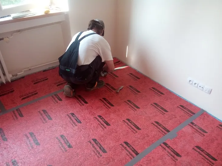 Montáž izolace pod koberec v prázdné místnosti.