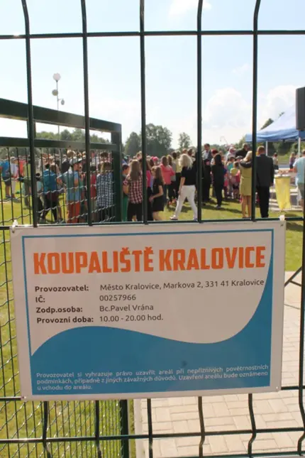 Informační tabule koupaliště v Královicích za plotem.