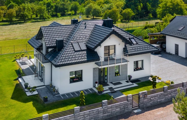 Moderní dům s tmavou keramickou střešní krytinou na pozadí zelené přírody.