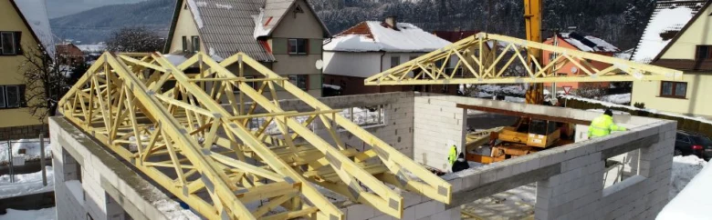 Montáž dřevěných vazníků na střeše budovy v zimním prostředí.