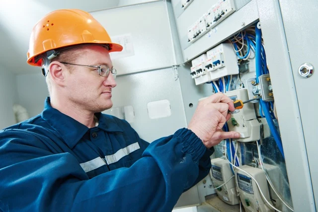 Elektrikář upravuje komponenty v průmyslovém rozvaděči.