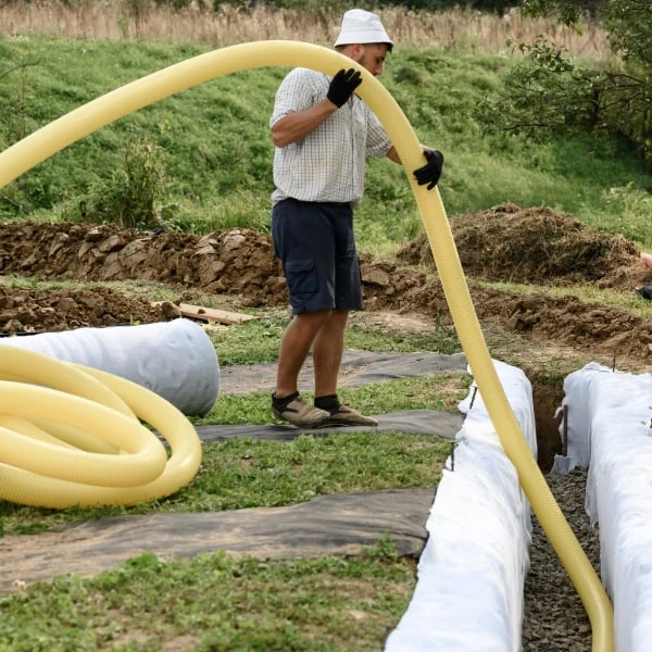 Muž instaluje žluté drenážní trubky do příkopu kolem domu.
