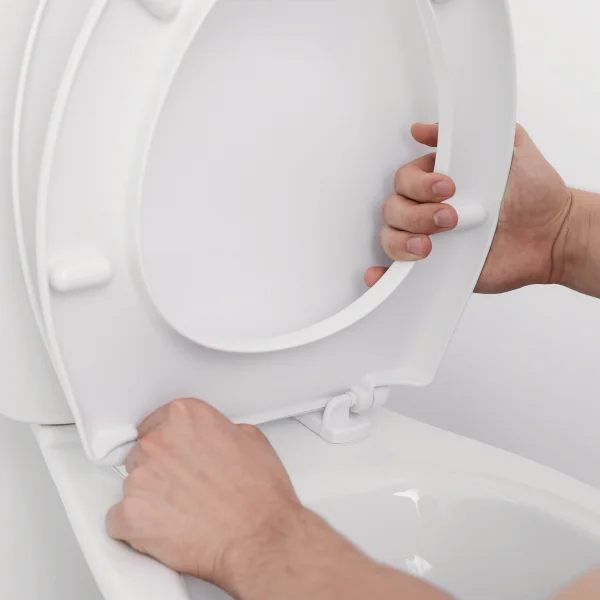ruce nastavují bílé WC prkénko na mísu
