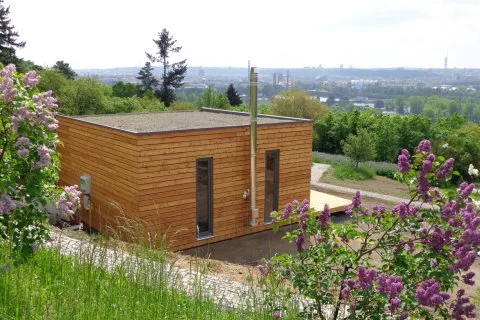 Moderní dřevěná modulární chata na svahu s kvetoucími liliovými keři.