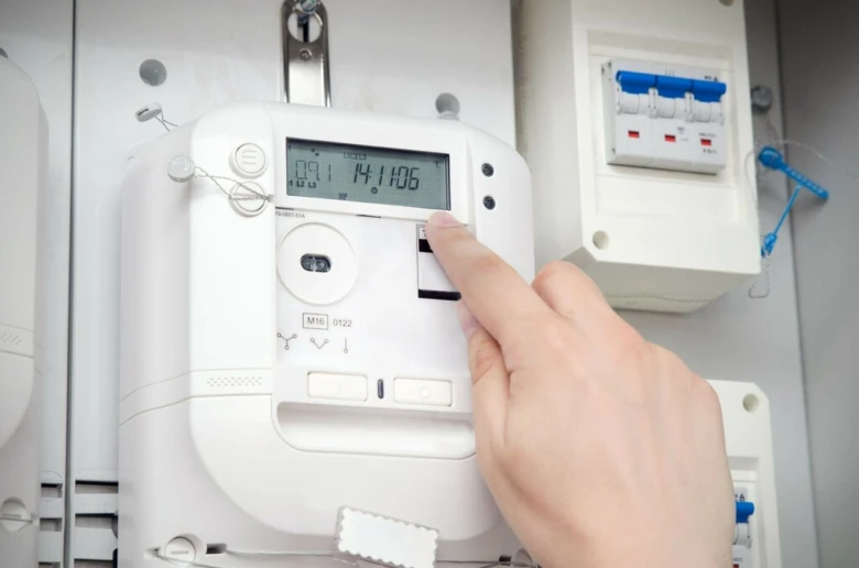 Ruka tlačí na displej elektroměru pro zobrazení spotřeby.