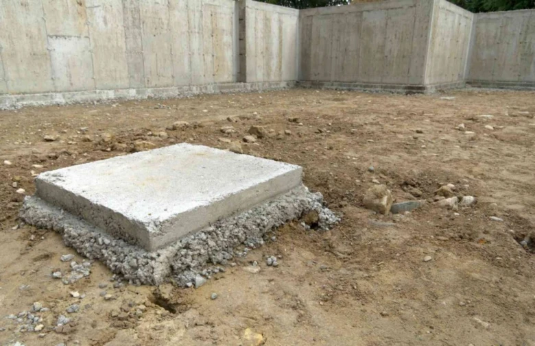 Čerstvě nalitý betonový základ pro dřevostavbu na štěrkovém podkladu.