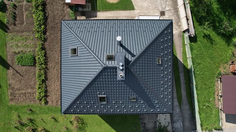 Pohled shora na dokončenou montáž tmavě šedé plechové střechy.