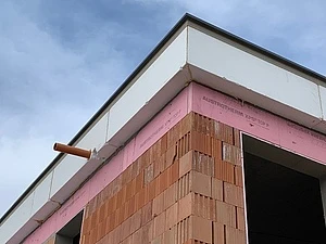 Detail atiky střechy s izolací mezi cihlovou zdí.