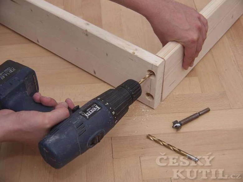 Montáž dřevěného rámu postele vrtáním otvorů pro spojovací prvky.