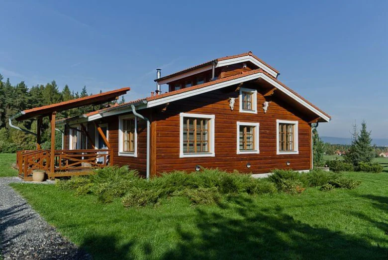 Tradiční dřevěný domek s šikmou střechou na trávníku.