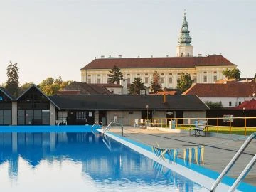 Venkovní bazén v Kroměříži s historickou budovou na pozadí.