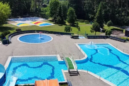 Více bazénů s kluzišti v areálu koupaliště obklopeném zelení.