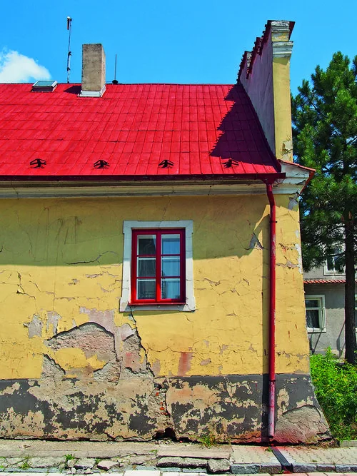 Žlutý dům s odškrceným omítkou a trhlinami ve zdivu.