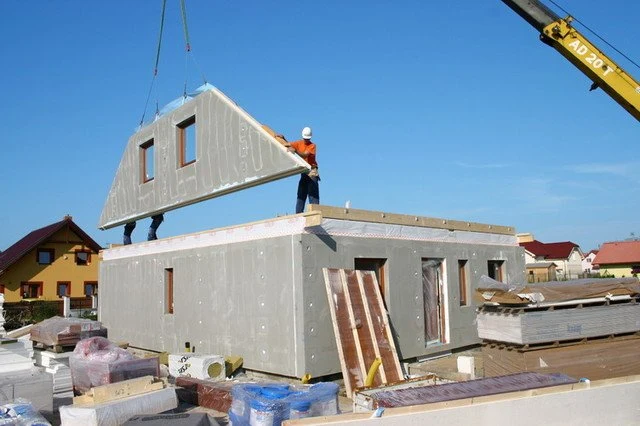 Montáž prefabrikovaného dřevěného domu s kranem na staveništi.