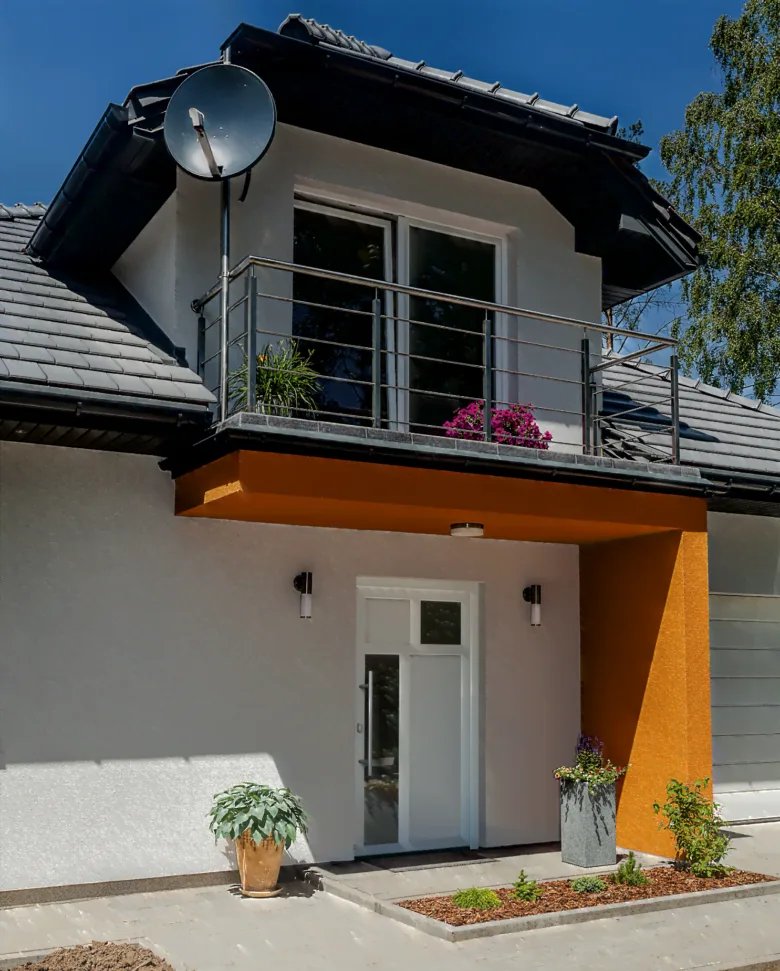 Moderní bílé vstupní dveře do domu pod lodžií s květinami.