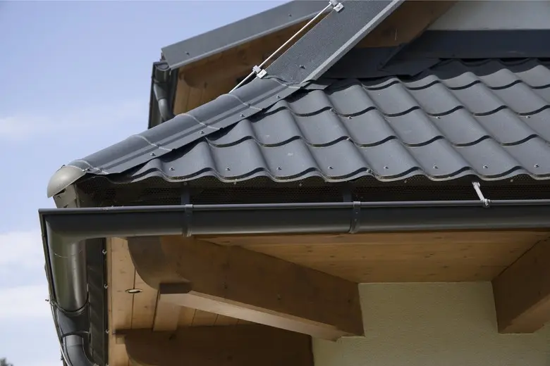 Detailní pohled na montáž plechové střechy s taškami a okapem.