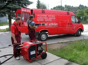 Dva pracovníci u generátoru s nápisem na kamionu pro vložkování komínů.