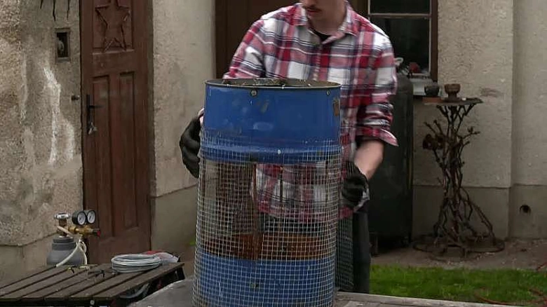 Muž drží modrou barel s mřížkou pro prosévání zeminy.