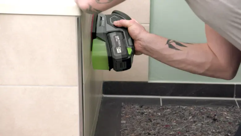 Člověk čistí spáry mezi dlaždicemi v koupelně pomocí elektrického nástroje.