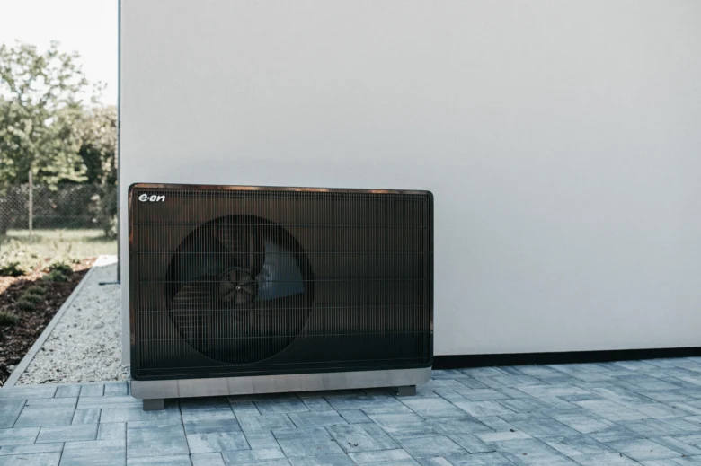 Venkovní tepelné čerpadlo s viditelným ventilátorem u bílé zdi.