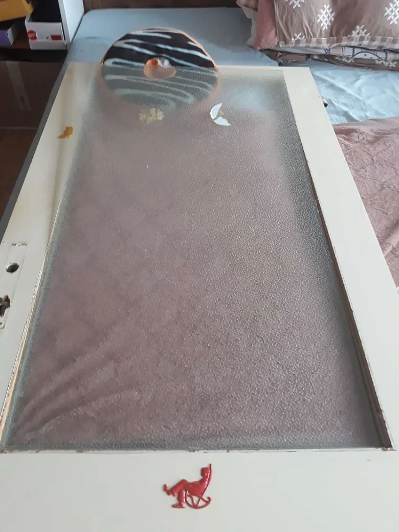 Skleněná výplň do dveří s bílým rámem ležící na posteli.
