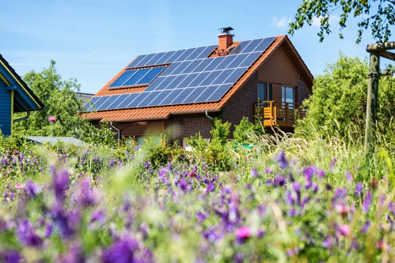 Dům s fotovoltaickými panely na střeše v zelené krajině.