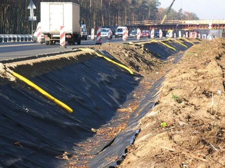 Instalace černé nopové folie na svahu silnice s žlutými hřebíky.