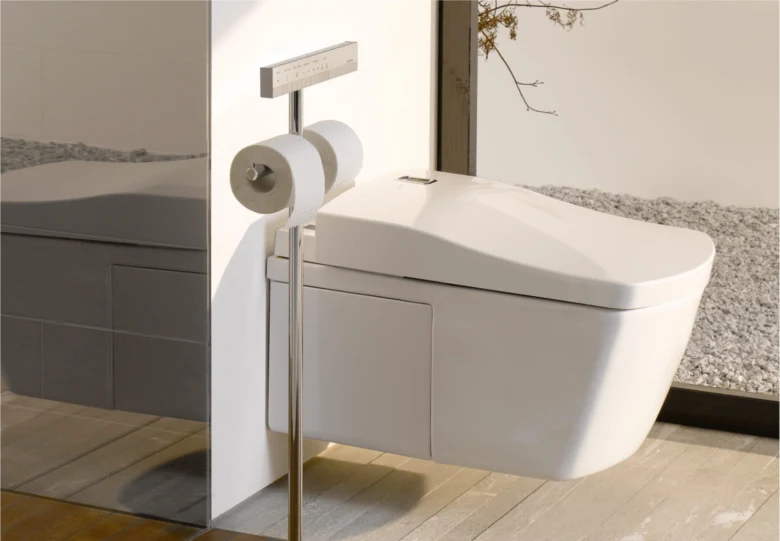 Moderní záchod s bidet funkcemi v koupelně vedle držáku na toaletní papír.