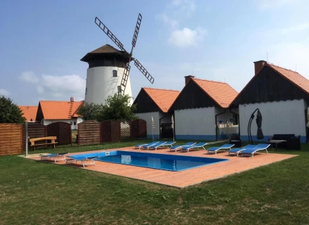 Bílý větrný mlýn vedle bazénu s lehátky v rekreačním areálu.