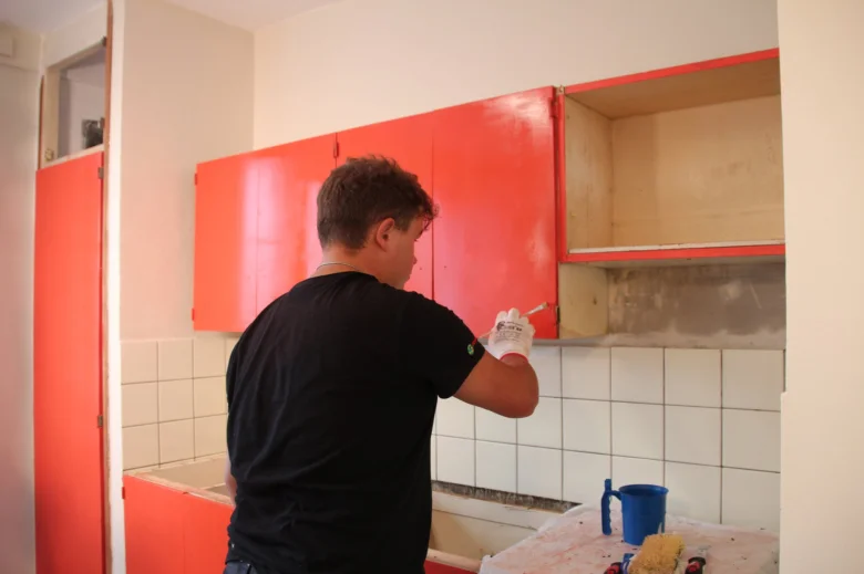 Muž maluje oranžové kuchyňské skříňky během renovace.