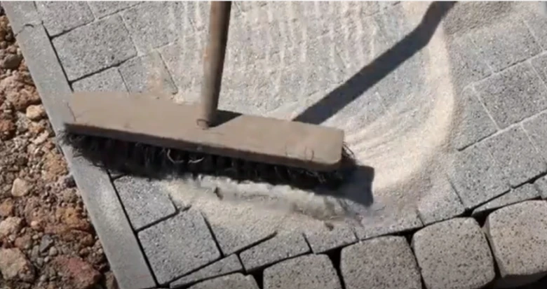 Štetec vysypává písek mezi dlaždice pro zámkovou dlažbu.