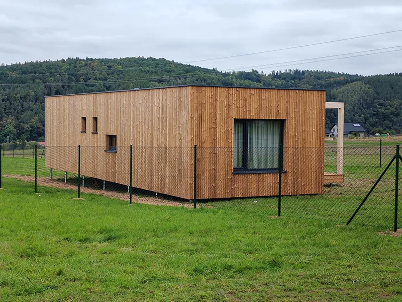Moderní dřevěný modulární dům stojí na trávníku v přírodě.