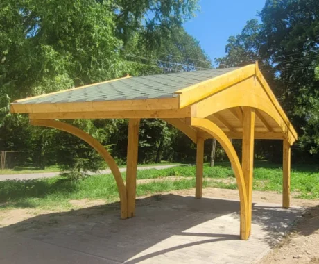 Dřevěný přístřešek s obloukovými nohami na venkovním prostranství.