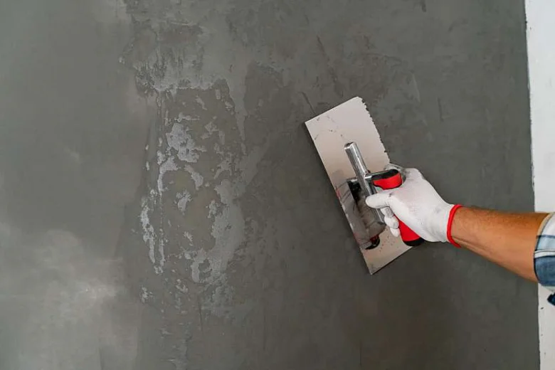 Ruční aplikace betonové stěrky na vnitřní zeď pomocí špachtle.