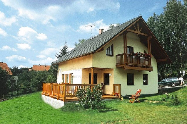 Dřevostavba s dřevěným balkonem na trávníku pod modrou oblohou.