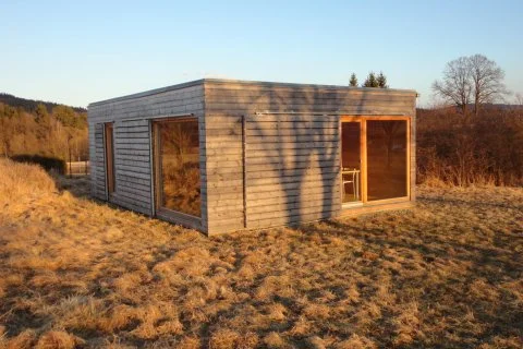 Moderní prefabrikovaný dřevěný dům stojí na travnatém svahu.