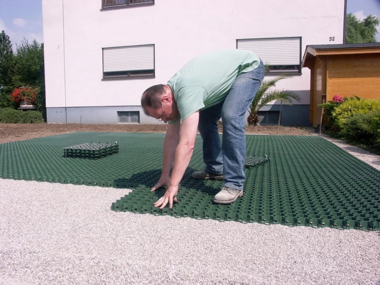 Muž pokládá zelené zatravňovací dlaždice na štěrkovou plochu.