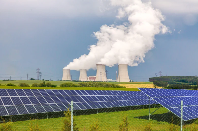Fotovoltaické panely na poli s elektrárnou v pozadí.